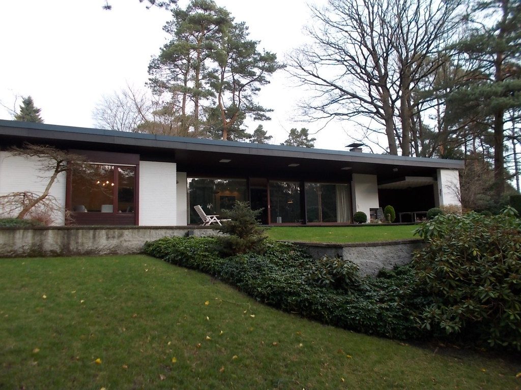 Flacher Bungalow mit großen Fenstern im Garten unter Kiefern
